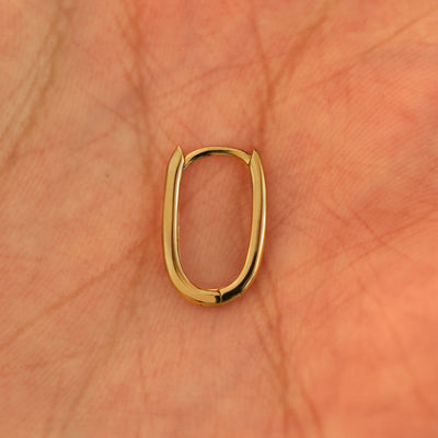 A single closed 14k yellow gold Oval Huggie Hoop resting in a model's palm