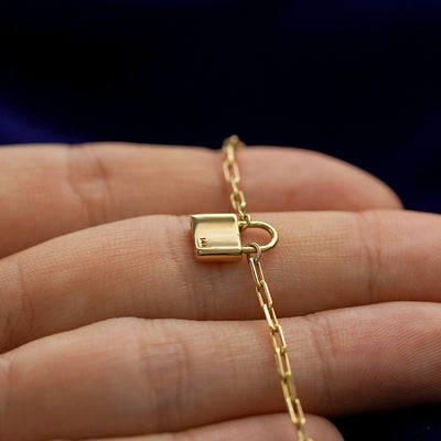 Back side view of a 14k gold padlock pendant necklace lying across a model's fingertips