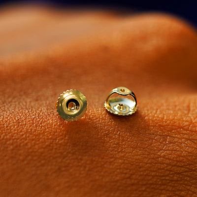 A pair of solid 14k gold screw back earring backings on the back of a hand