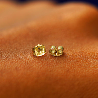 A pair of solid 14k gold standard push back earring backings on the back of a hand