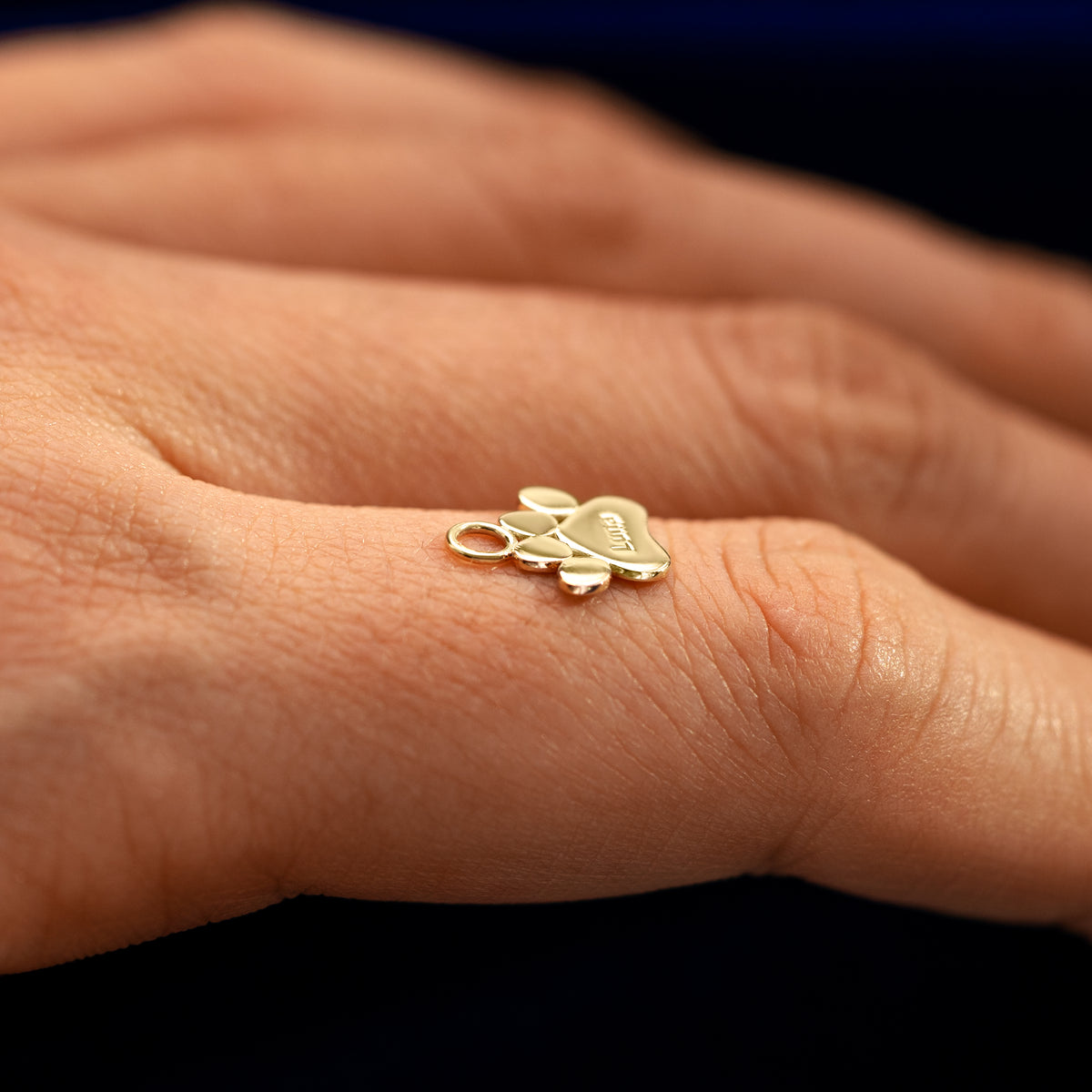 Side view of a for earring paw charm resting on a models finger to show the thickness of the charm