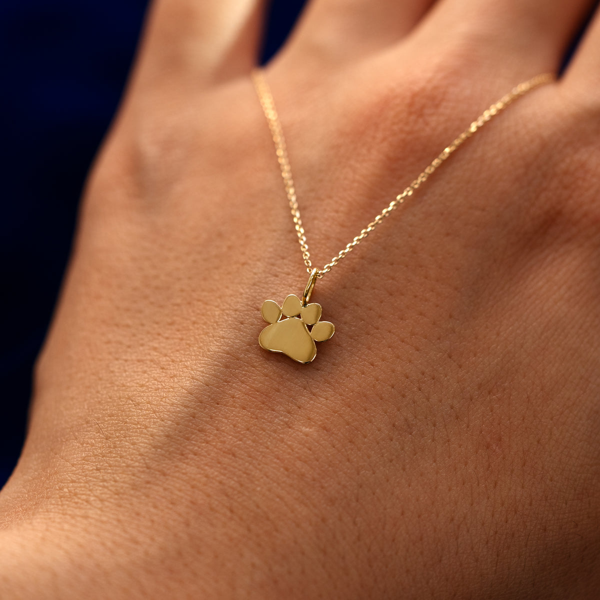 A solid 14k gold paw charm on a cable chain draped over the back of a models hand
