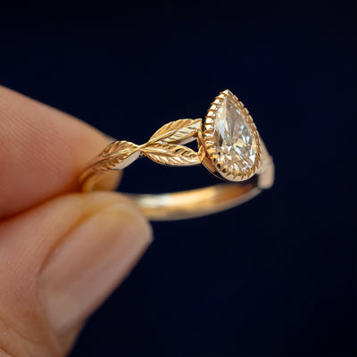 A model holding a Pear Clear Lab Diamond Leaves Ring tilted to show the side of the ring