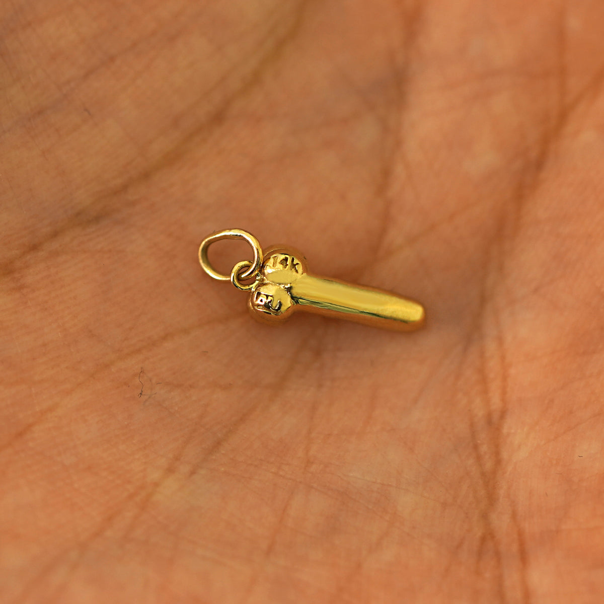 Another angle of a 14k yellow gold penis charm in the palm of a models hand