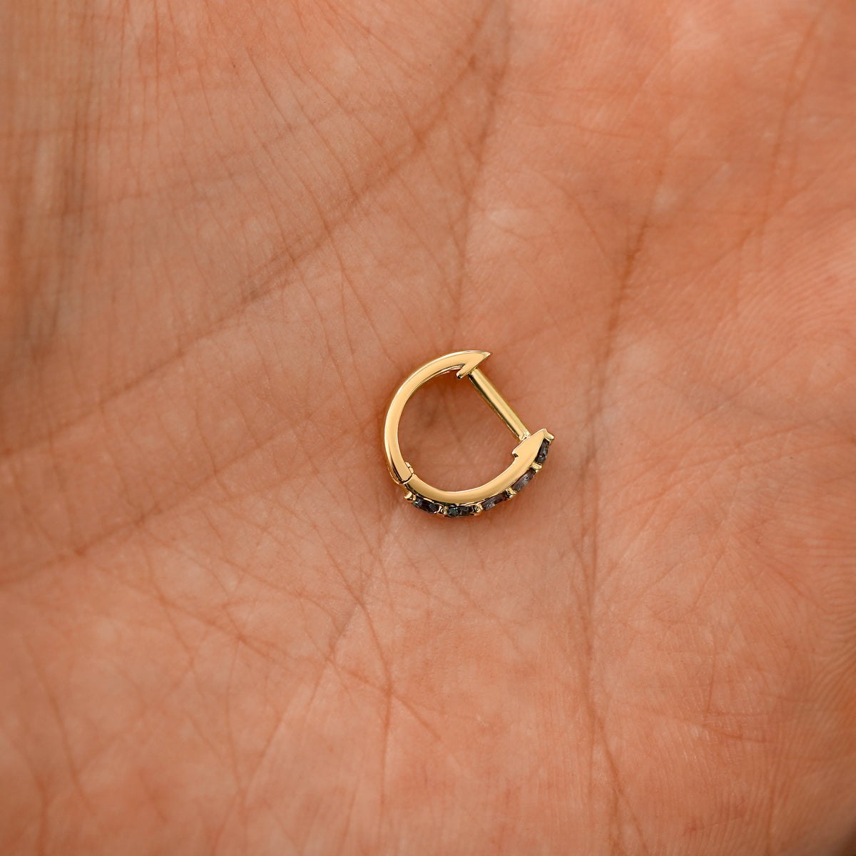 A closed rose cut salt and pepper diamond huggie hoop laying in a models palm