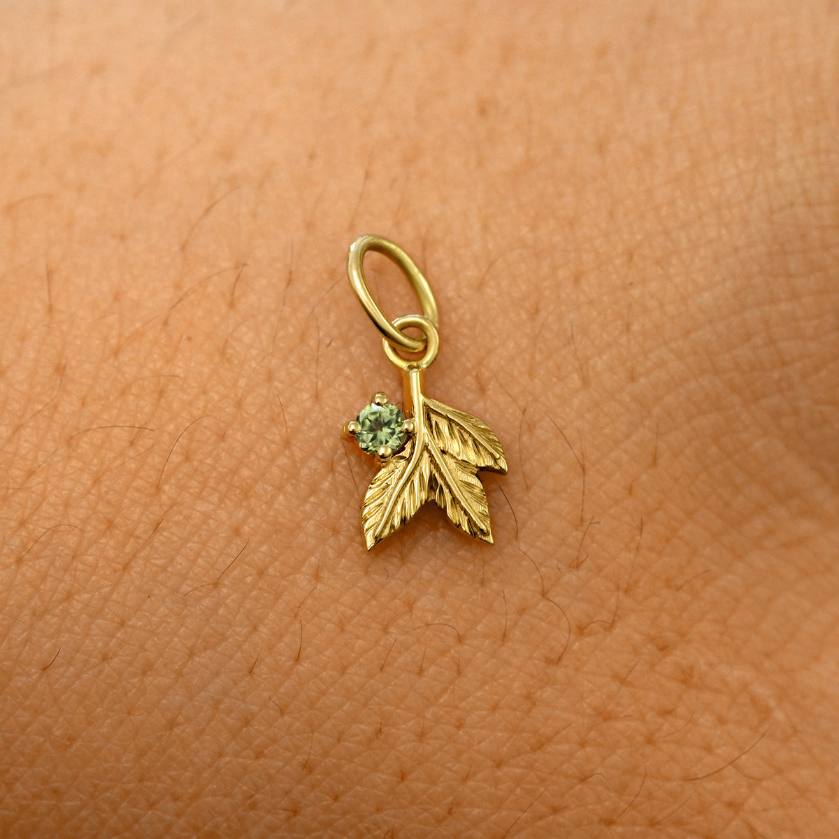 A solid 14k yellow gold peridot Gemstone 3 Leaves Charm resting on the back of a model's hand