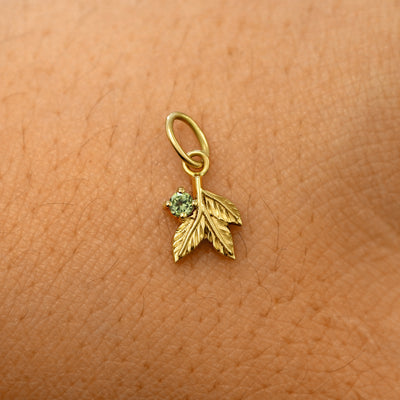 A solid 14k yellow gold peridot Gemstone 3 Leaves Charm resting on the back of a model's hand