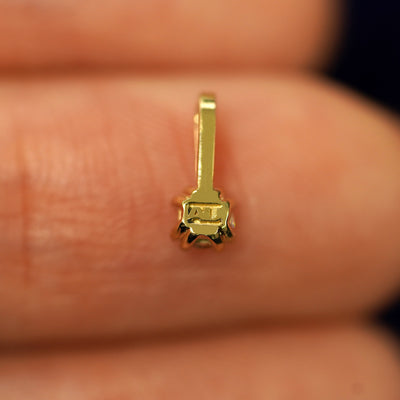 A solid gold Peridot Charm for chain facedown on a model's fingertip to show the solid back of the charm