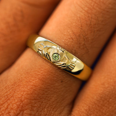 Close up view of a model's fingers wearing a 14k yellow gold peridot Gemstone Claddagh Band