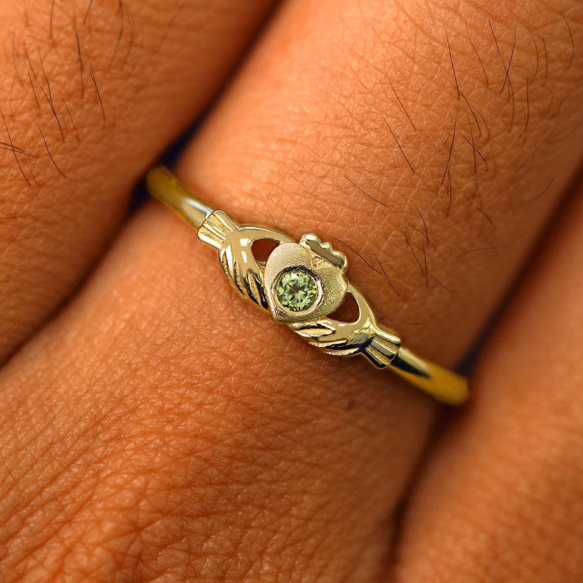 Close up view of a model's fingers wearing a 14k yellow gold peridot Thin Gemstone Claddagh Ring