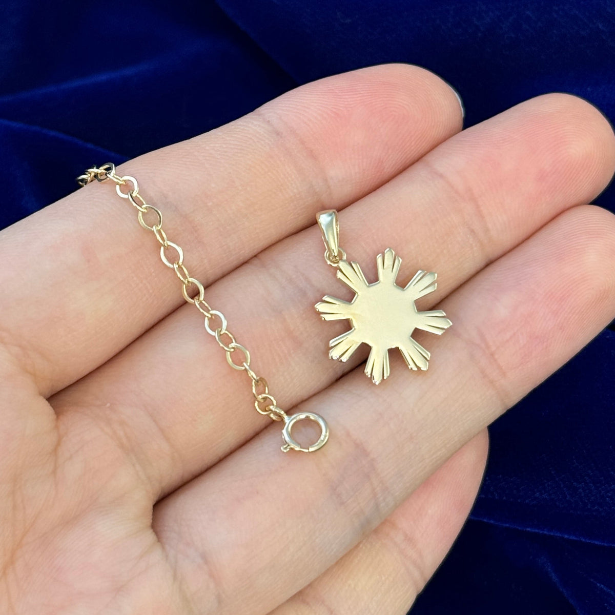 Yellow gold philippines sun charm pendant and custom chain extender resting on model's hand