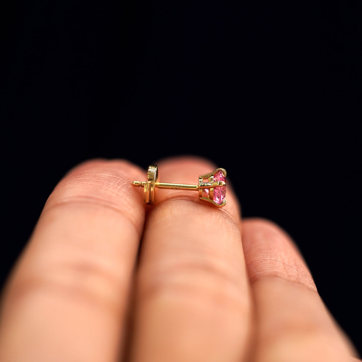 A 14k gold Pink Sapphire Pressure Lock Earring resting sideways on a model's fingertips to show detail