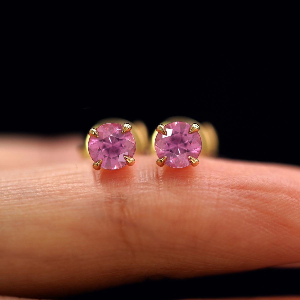A pair of solid yellow gold Pink Sapphire Pressure Lock Earrings resting on a model's fingertip