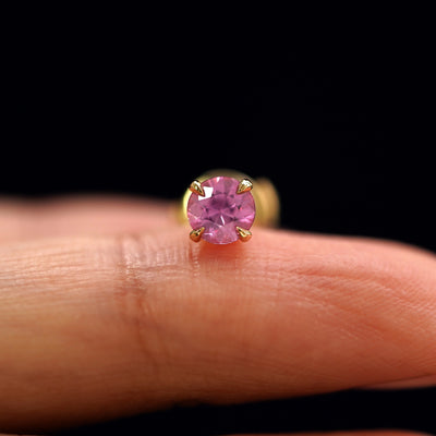 A 14k yellow gold Pink Sapphire Pressure Lock Earring resting on a model's fingertip
