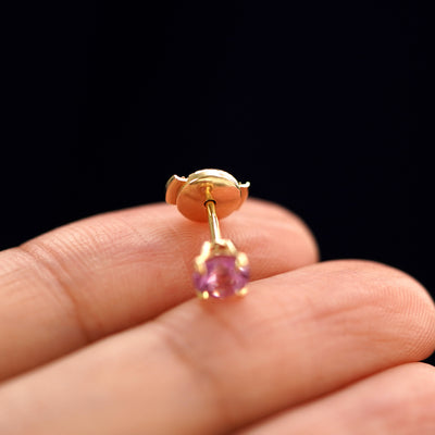 A solid gold Pink Sapphire Pressure Lock Earring tilted on a model's fingertip to show the pressure lock backing on the post