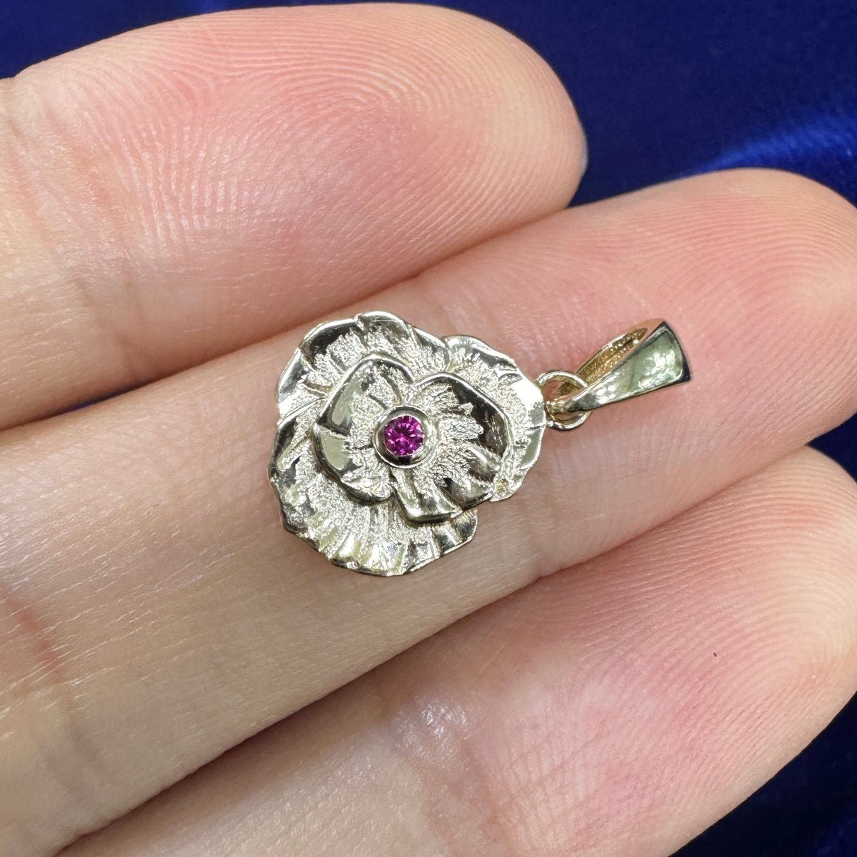 Poppy charm with tiny ruby in the center resting on model's hand
