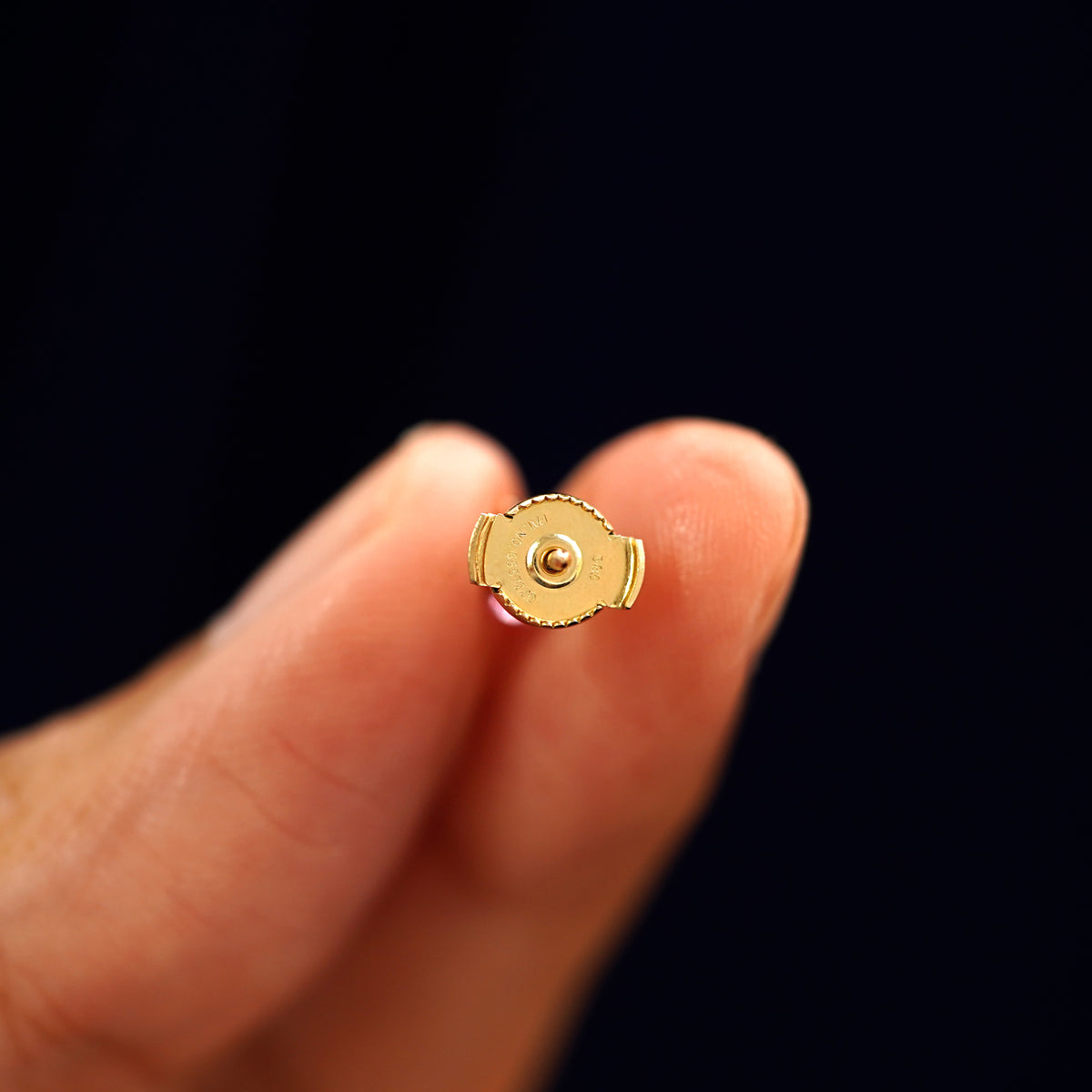 A 14k gold Pink Sapphire Pressure Lock Earring held backward between a model's fingers to show the backing