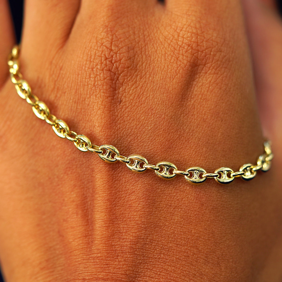 A solid gold Puffy Mariner Bracelet resting on the back of a model's hand