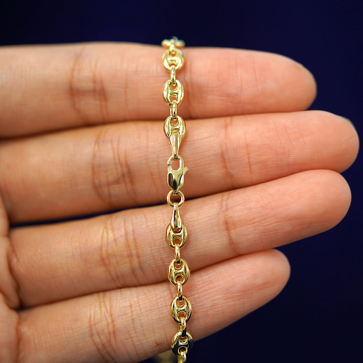 A model's hand holding a yellow 14k gold Puffy Mariner Bracelet with a lobster claw clasp