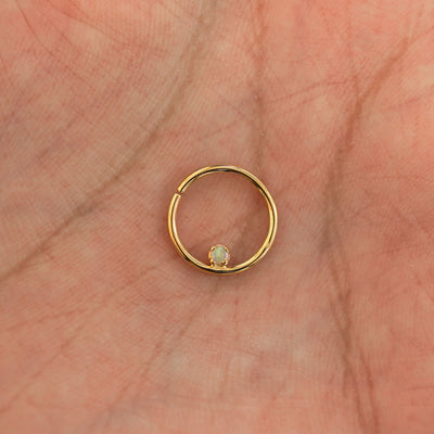 A model's hand holding a 14 karat yellow gold opal Pierced Raised Gemstone Septum