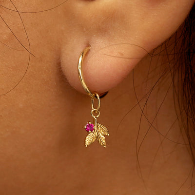 Close up view of a model's ear wearing a yellow gold ruby Gemstone 3 Leaves Charm on a Small Seamless Huggie Hoop