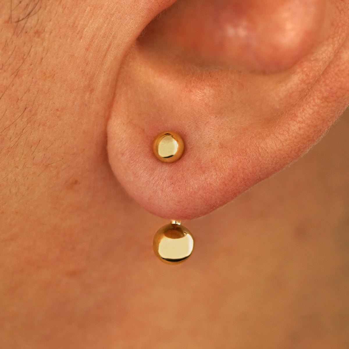 Close up view of a model's ear wearing a 14k yellow gold Large Curved Barbell through a lobe piercing