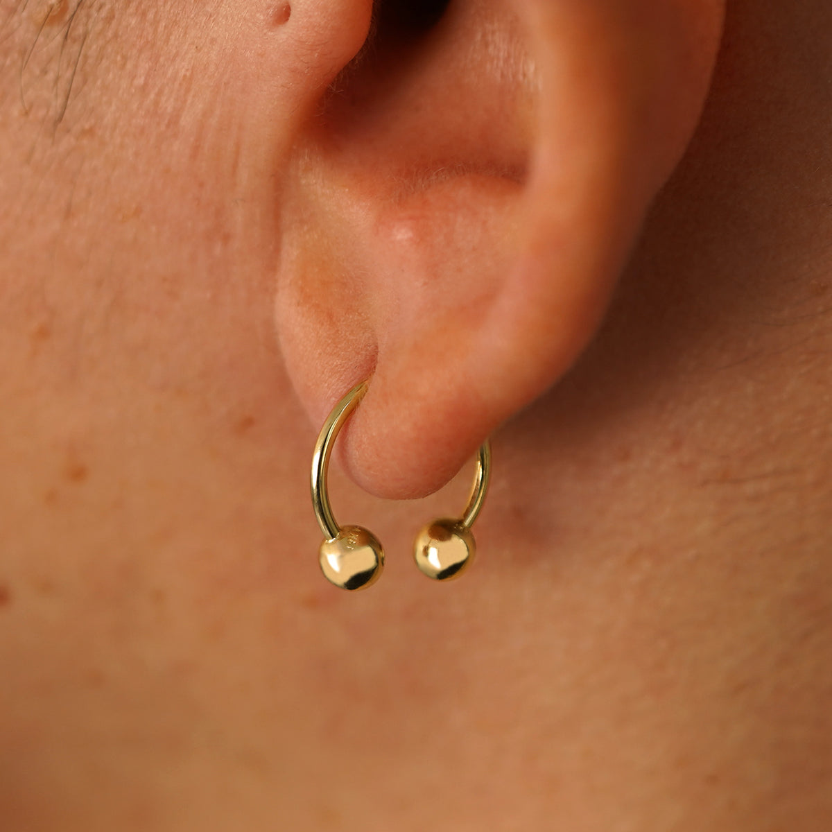 Close up view of a model's ear wearing a 14k yellow gold Medium Horseshoe  through a lobe piercing