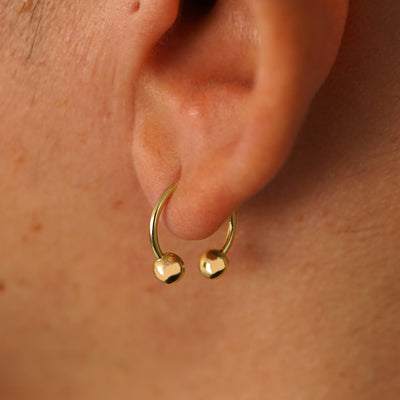 Close up view of a model's ear wearing a 14k yellow gold Medium Horseshoe  through a lobe piercing