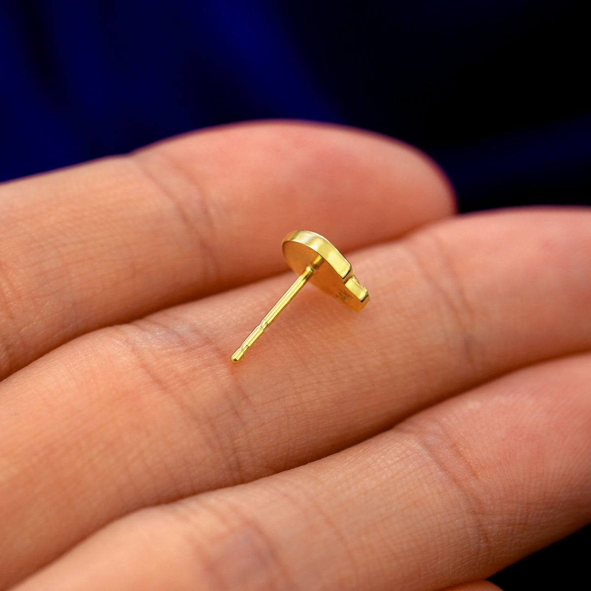 A 14k gold Skull Earring in a model's hand resting on its side to show the thickness of the earring 