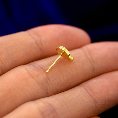 A 14k gold Skull Earring in a model's hand resting on its side to show the thickness of the earring 