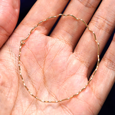 A yellow gold Wave Bangle Bracelet sitting in a model's palm