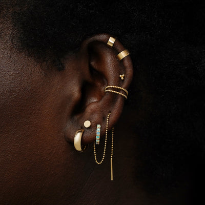 A model wearing a small opal huggie hoop with other yellow gold earrings and ear cuffs