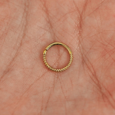 A model's hand holding a 14 karat yellow gold Pierced Rope Septum