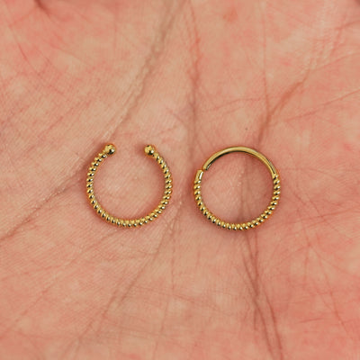 Two 14k solid gold Rope Septum rings show in options of Non-Pierced and Pierced resting in the palm of a model's hand