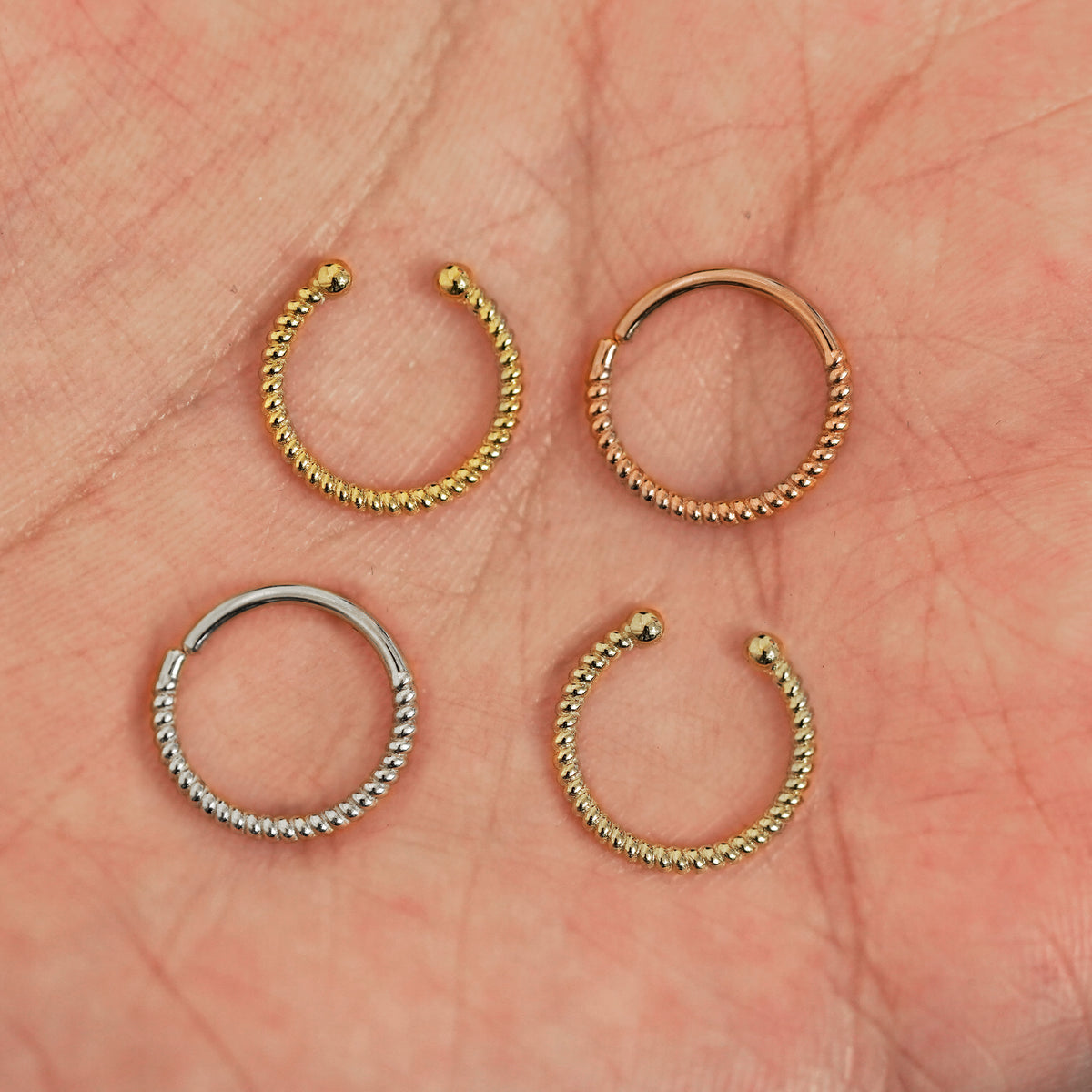 Four versions of the Rope Septum shown in options of yellow, white, rose and champagne gold in a model's palm