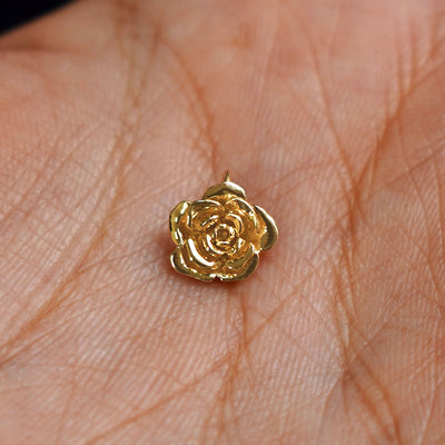 A solid gold Rose Charm for chain resting in a model's palm
