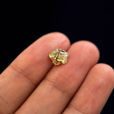 A yellow gold Rose Earring laying facedown on a model's fingers to show the underside view