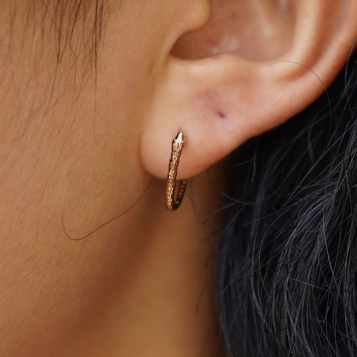 Close up view of a model's ear wearing a rose gold Snake Hoop / Piercing