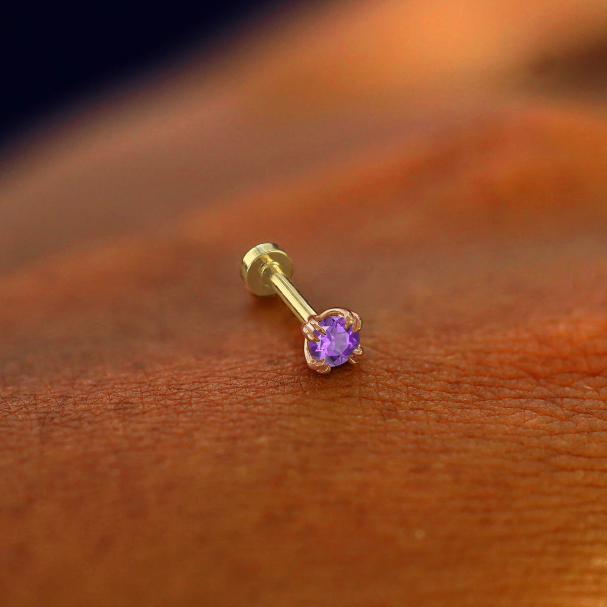 A solid 14k rose gold Amethyst Flatback Piercing resting on the back of a model's hand