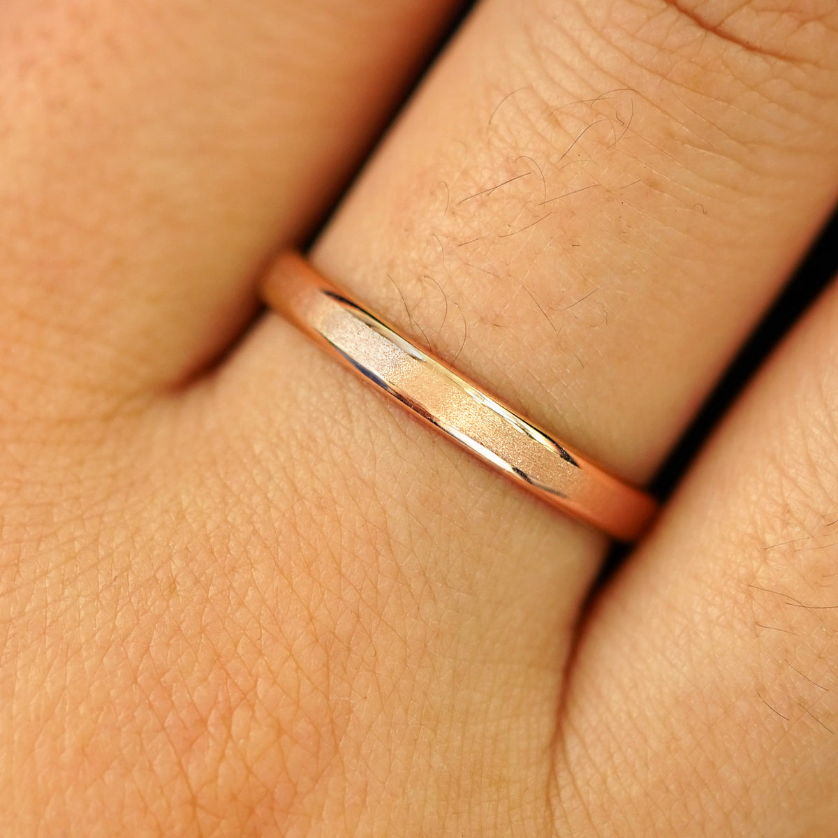 Close up view of a model's hand wearing a solid rose gold Beveled Edge Band