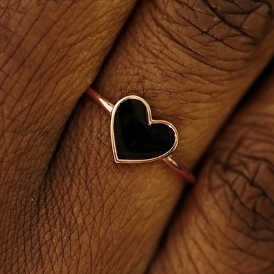 Close up view of a model's fingers wearing a 14k rose gold black enamel heart ring