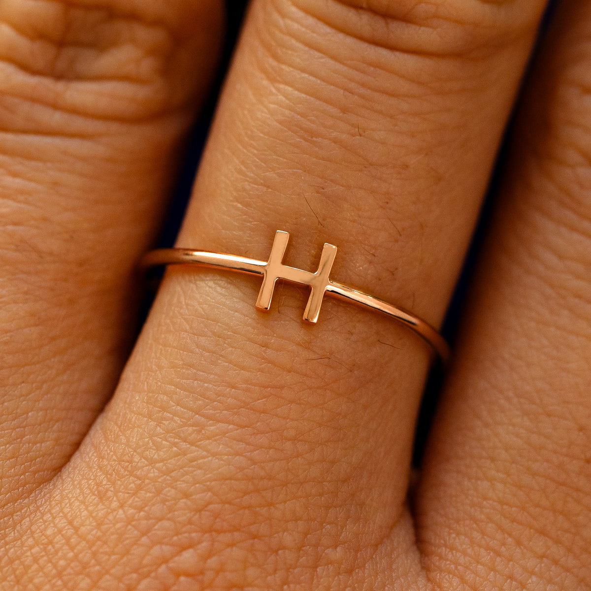 Close up view of a model's fingers wearing a 14k rose gold block initial Ring with the letter H