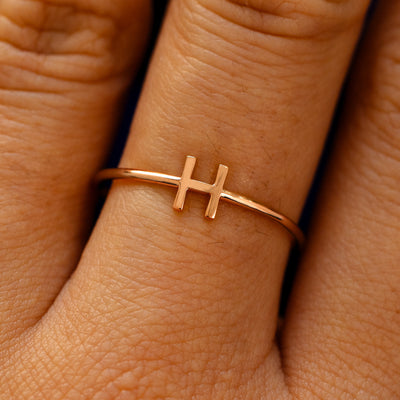 Close up view of a model's fingers wearing a 14k rose gold block initial Ring with the letter H