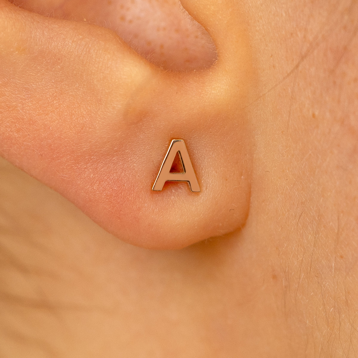 Close up view of a models ear wearing a 14k rose gold letter A block initial stud earring