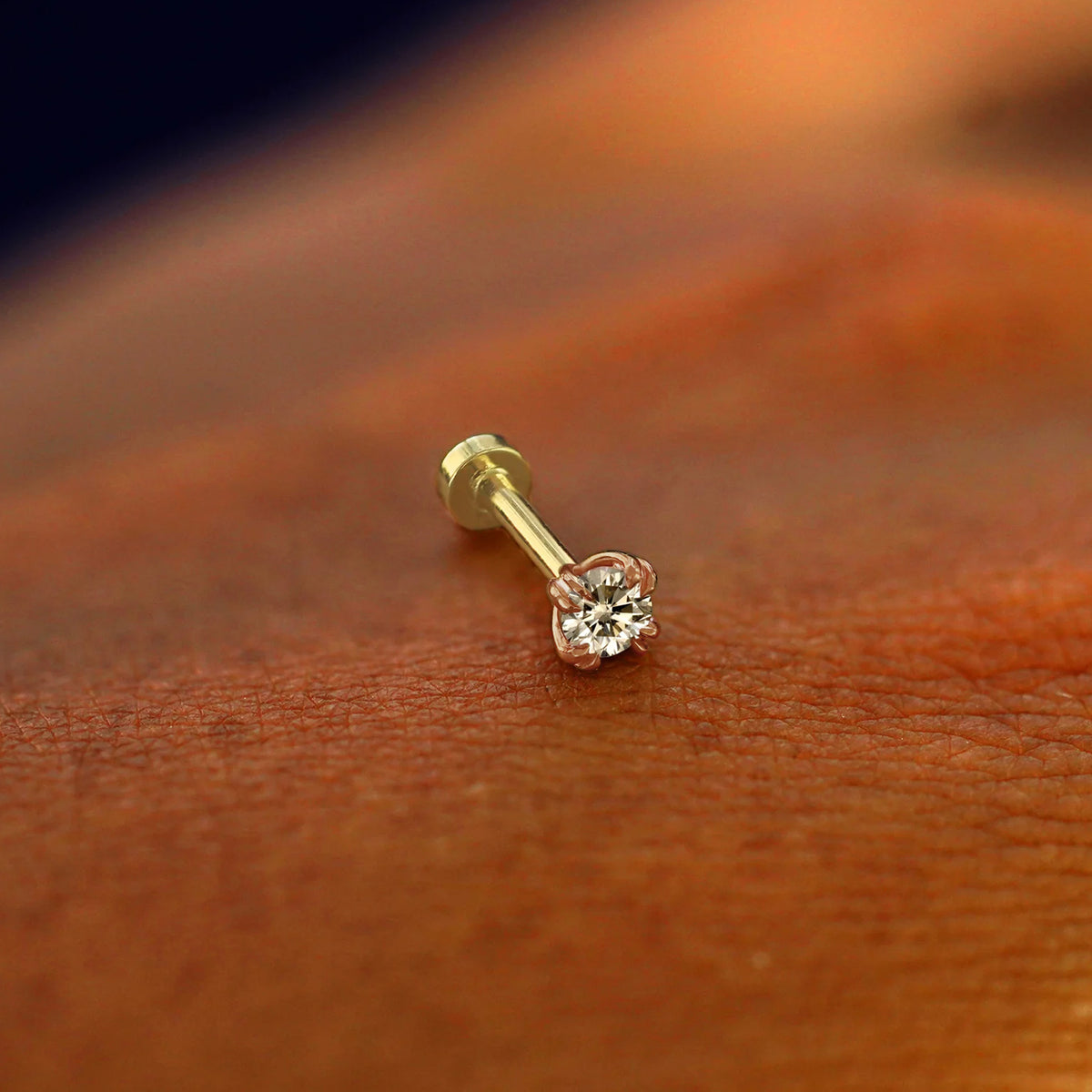 A solid 14k rose gold Champagne Diamond Flatback Piercing resting on the back of a model's hand