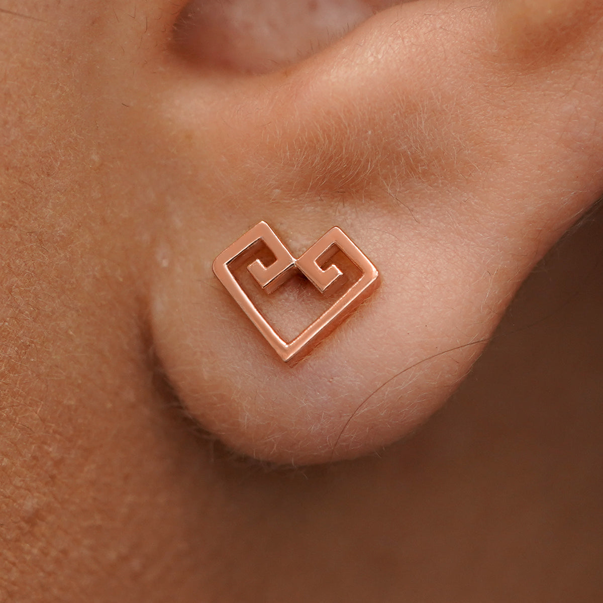 Close up view of a model's ear wearing a rose gold Chere Heart Earring