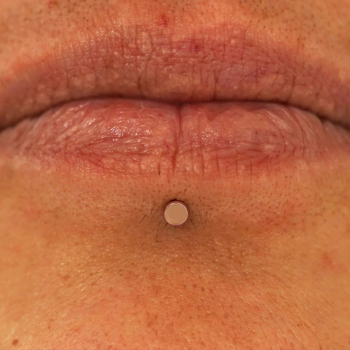 Close up view of a model's lips wearing a 14k rose gold Mini Circle Flatback in a labret piercing