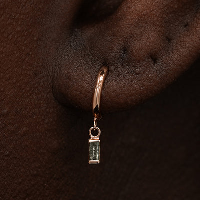 Close up view of a model's ear wearing a rose gold Baguette Diamond Dangle Huggie Hoop