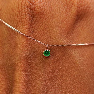 Close up view of a 14k rose gold Emerald Necklace draped across the back of a model's hand