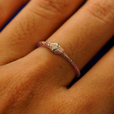 Close up view of a model's hand wearing a rose gold emerald Gemstone Ouroboros Snake Ring